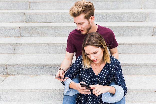 Pareja joven seria sentado en la escalera mirando el teléfono móvil