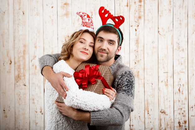 Pareja joven sonriendo abrazando la celebración de regalo de Navidad sobre superficie de madera