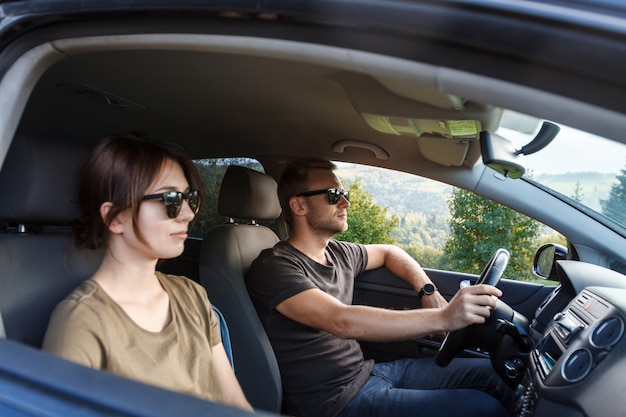 Pareja joven sonriendo, sentado en el coche, disfrutando de vistas a las montañas