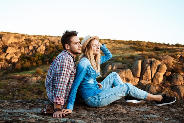 Pareja joven sonriendo, sentado en la roca en el cañón, disfrutando de la vista