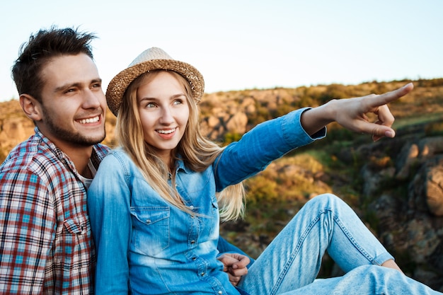 Pareja joven sonriendo, sentado en la roca en el cañón, disfrutando de la vista