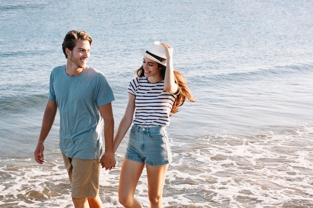 Pareja joven sonriente andando por la orilla