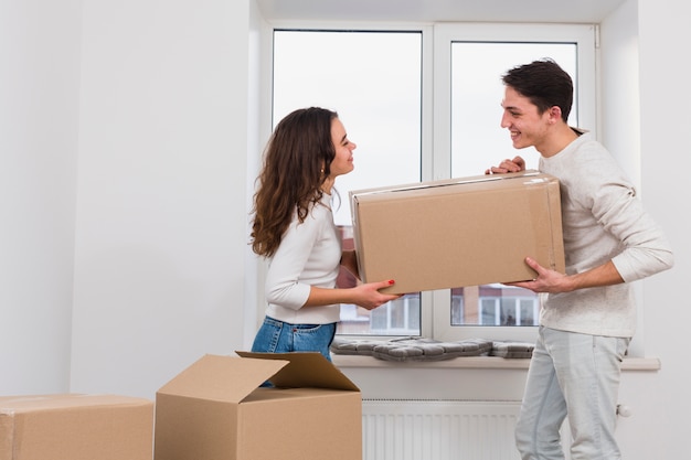 Pareja joven sonriente con caja de cartón en nuevo apartamento