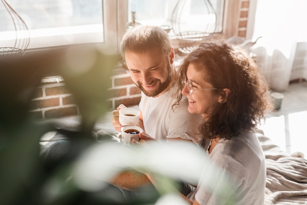 Foto gratuita pareja joven sonriente cariñosa que sostiene la taza de café en manos