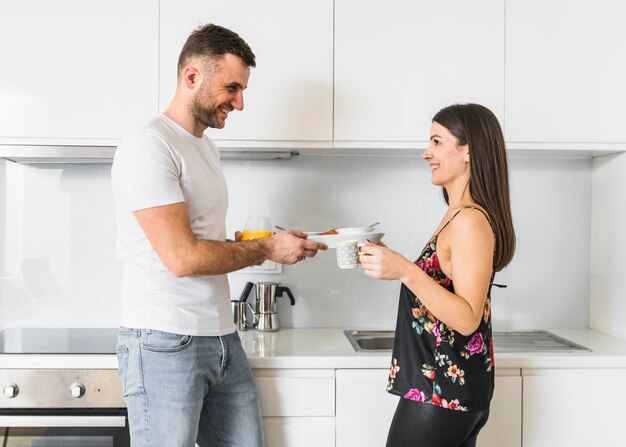 Pareja joven sonriente desayunando en la cocina