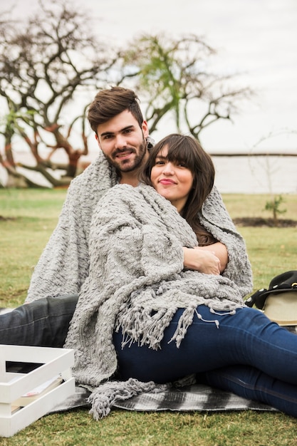 Pareja joven sonriente envuelta en una manta gris en picnic