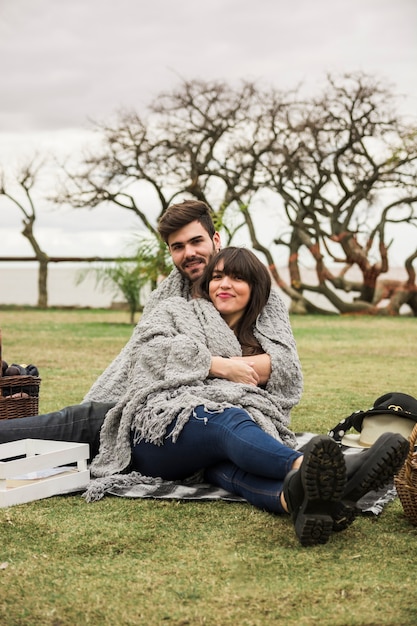 Pareja joven sonriente envuelta en una manta gris sentada en el jardín