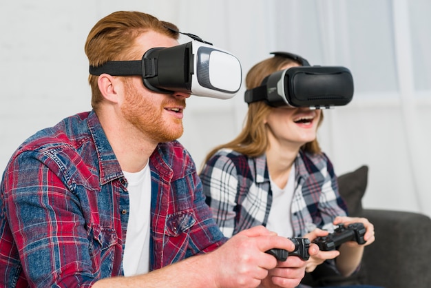 Pareja joven sonriente con gafas de realidad disfrutando de jugar el videojuego