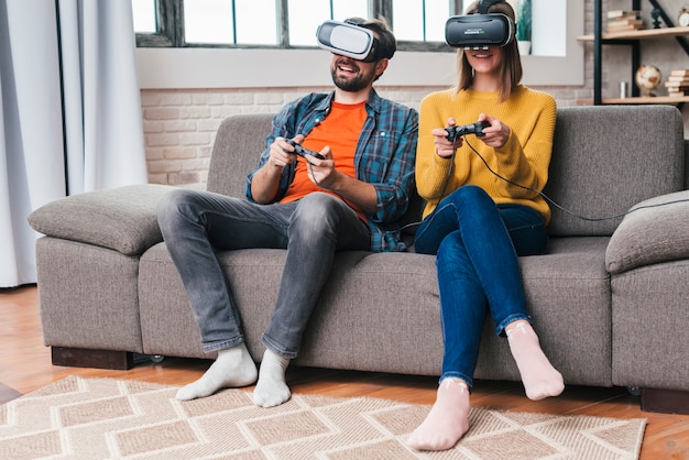 Foto gratuita pareja joven sonriente con las gafas de realidad virtual jugando al videojuego