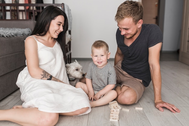 Pareja joven sonriente jugando con su hijo y su perro en casa