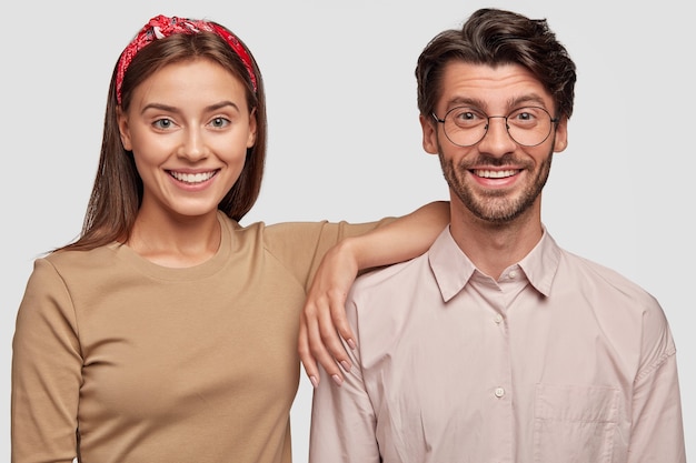 Pareja joven sonriente posando contra la pared blanca