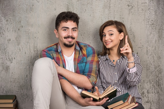 pareja joven sonriente sentada en el suelo con libros