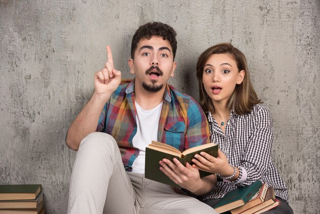 pareja joven sonriente sentada en el suelo con libros