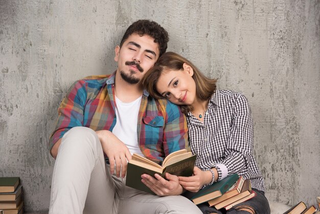 pareja joven sonriente sentada en el suelo con libros