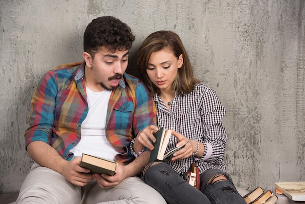 Foto gratuita pareja joven sonriente sentada en el suelo con libros