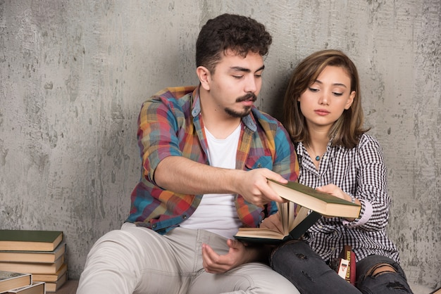 Foto gratuita pareja joven sonriente sentada en el suelo con libros