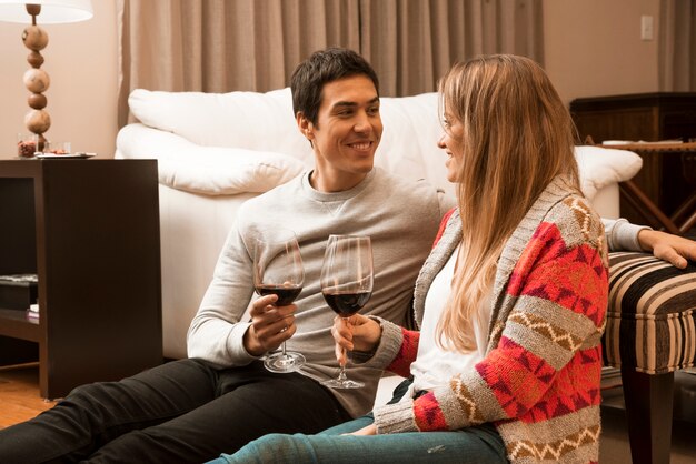 Pareja joven sonriente sosteniendo copas de vino en la sala de estar