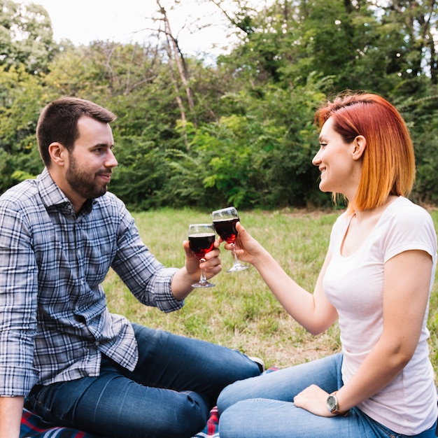 Foto gratuita pareja joven sonriente tostado copas sentado en el parque