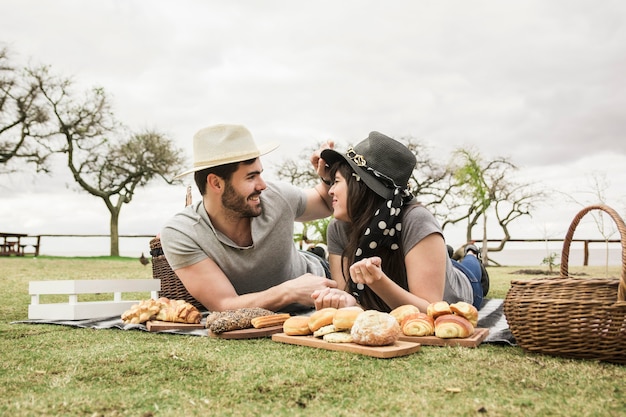 Pareja joven sonriente tumbado en una manta con panes horneados en el parque