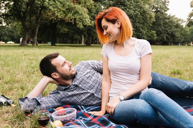 Pareja joven sonriente tumbado en manta sobre hierba verde con muchas frutas