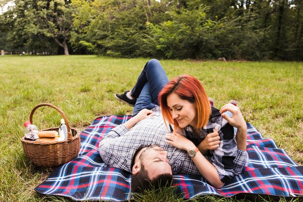 Pareja joven sonriente tumbado en manta sobre hierba verde en picnic