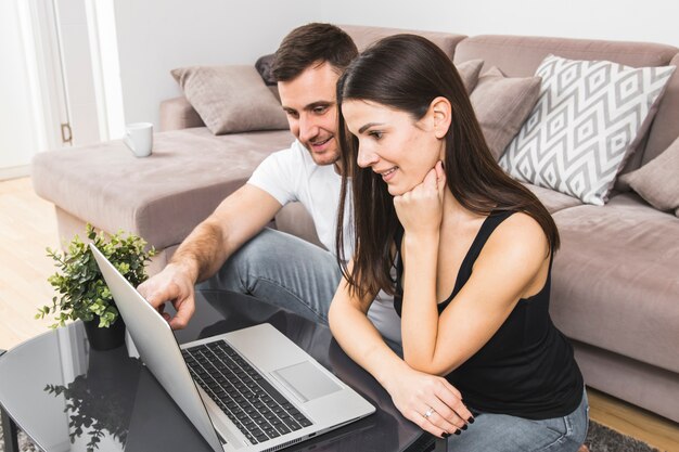 Pareja joven sonriente usando laptop en casa