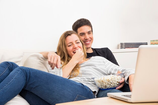 Pareja joven sonriente viendo la película en la computadora portátil