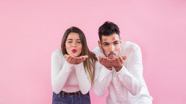 Pareja joven soplando besos sobre fondo rosa