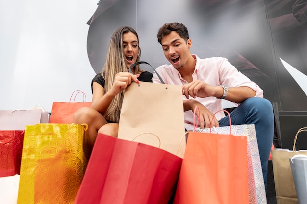 Foto gratuita pareja joven sorprendida mirando dentro de bolsas de compras