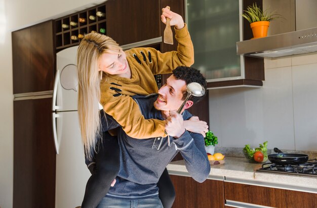 Pareja joven sosteniendo espátula y cucharón luchando juntos