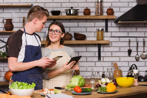 Pareja joven con tabletas digitales cocinando juntos