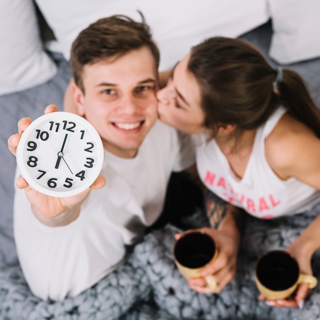 Foto gratuita pareja joven con tazas de café mostrando reloj con 6 am