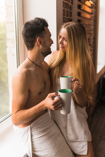 Pareja joven en toalla con taza de café cerca de la ventana