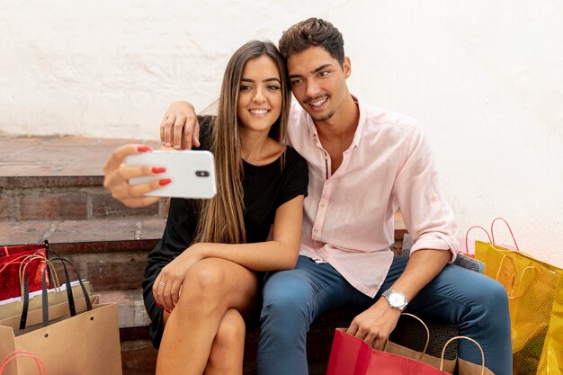 Pareja joven tomando selfies junto a bolsas de compras