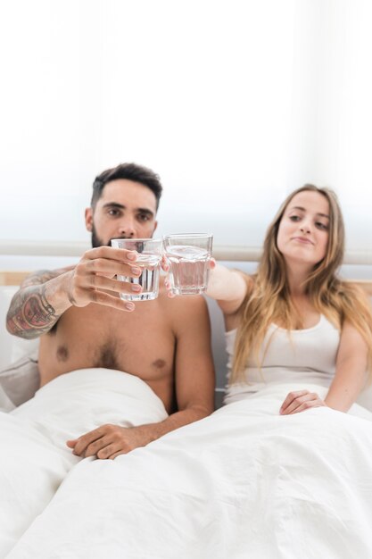 Pareja joven tostado vaso de agua en la cama