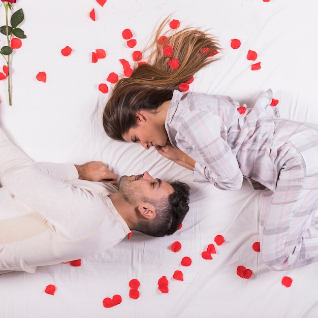 Foto gratuita pareja joven tumbado en la cama con pétalos de rosa