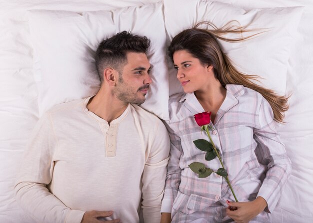 Pareja joven tumbado en la cama con rosa