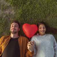 Foto gratuita pareja joven tumbado en la hierba con globo de corazón