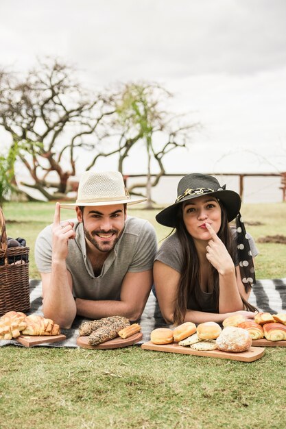 Pareja joven tumbado en la manta apuntando el dedo en picnic en el parque