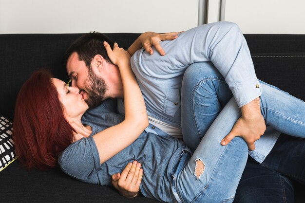 Foto gratuita pareja joven tumbado en el sofá besándose