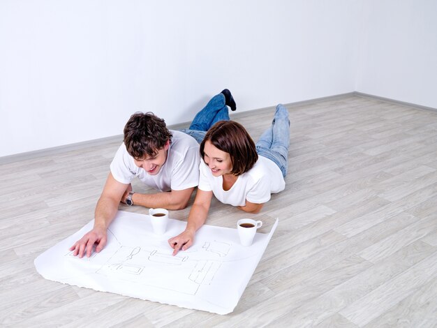 Pareja joven tumbado en el suelo y mirando el plan de habitación