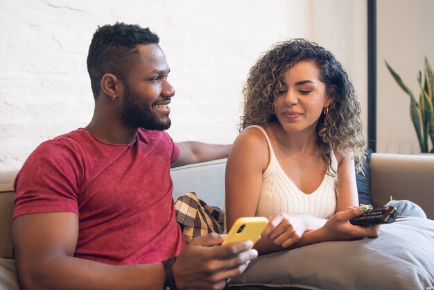 Pareja joven usando un teléfono móvil juntos mientras está sentado en un sofá en casa.