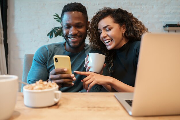 Pareja joven usando un teléfono móvil mientras desayunan juntos en casa.