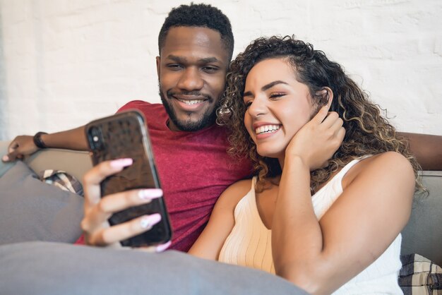 Pareja joven usando un teléfono móvil mientras está sentado en el sofá en casa. Quédate en casa. Nuevo concepto de estilo de vida normal.