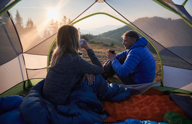 Pareja joven viajeros bebiendo café durante el viaje de campamento en las montañas