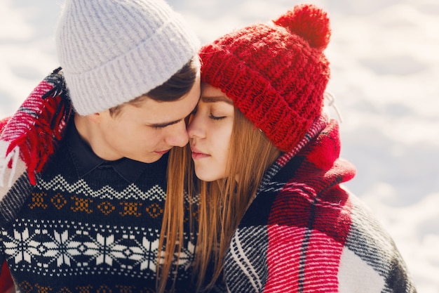 Foto gratuita pareja joven vistiendo una manta en un campo cubierto de nieve