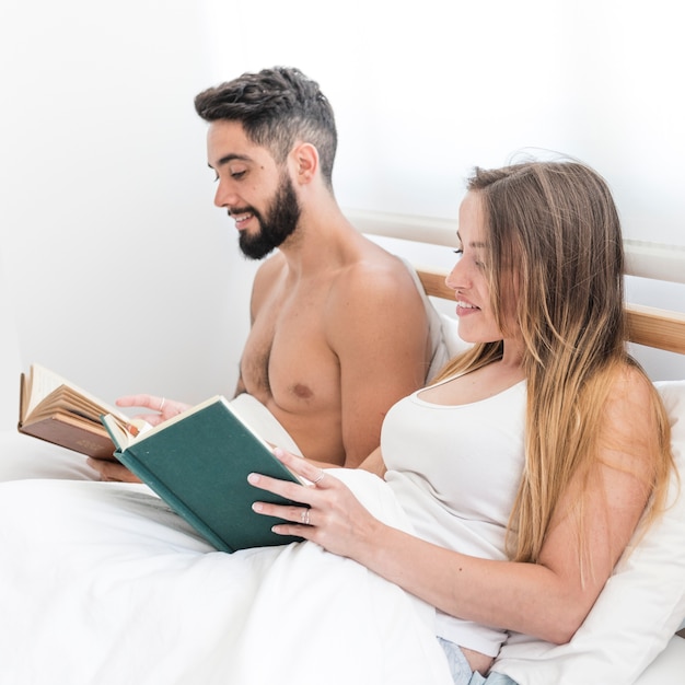 Pareja de jóvenes sentados en la cama leyendo el libro