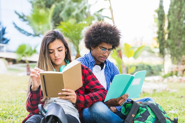 Pareja de jóvenes sentados juntos en el césped leyendo un libro en el parque al aire libre