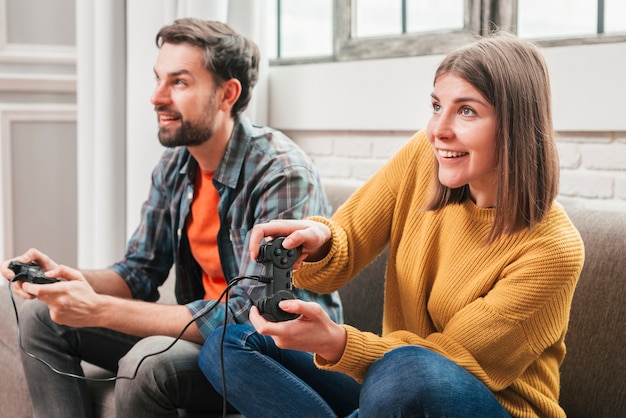 Pareja de jóvenes sentados en el sofá disfrutando jugando al videojuego