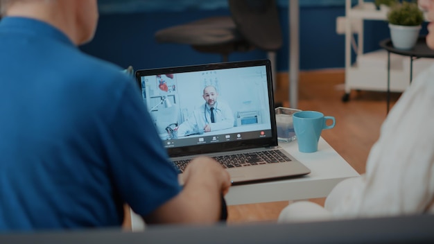 Pareja jubilada haciendo consulta en línea sobre videollamada con médico. Personas mayores que usan una computadora portátil para reunirse con un médico en una videoconferencia, hablando sobre atención médica en telemedicina.